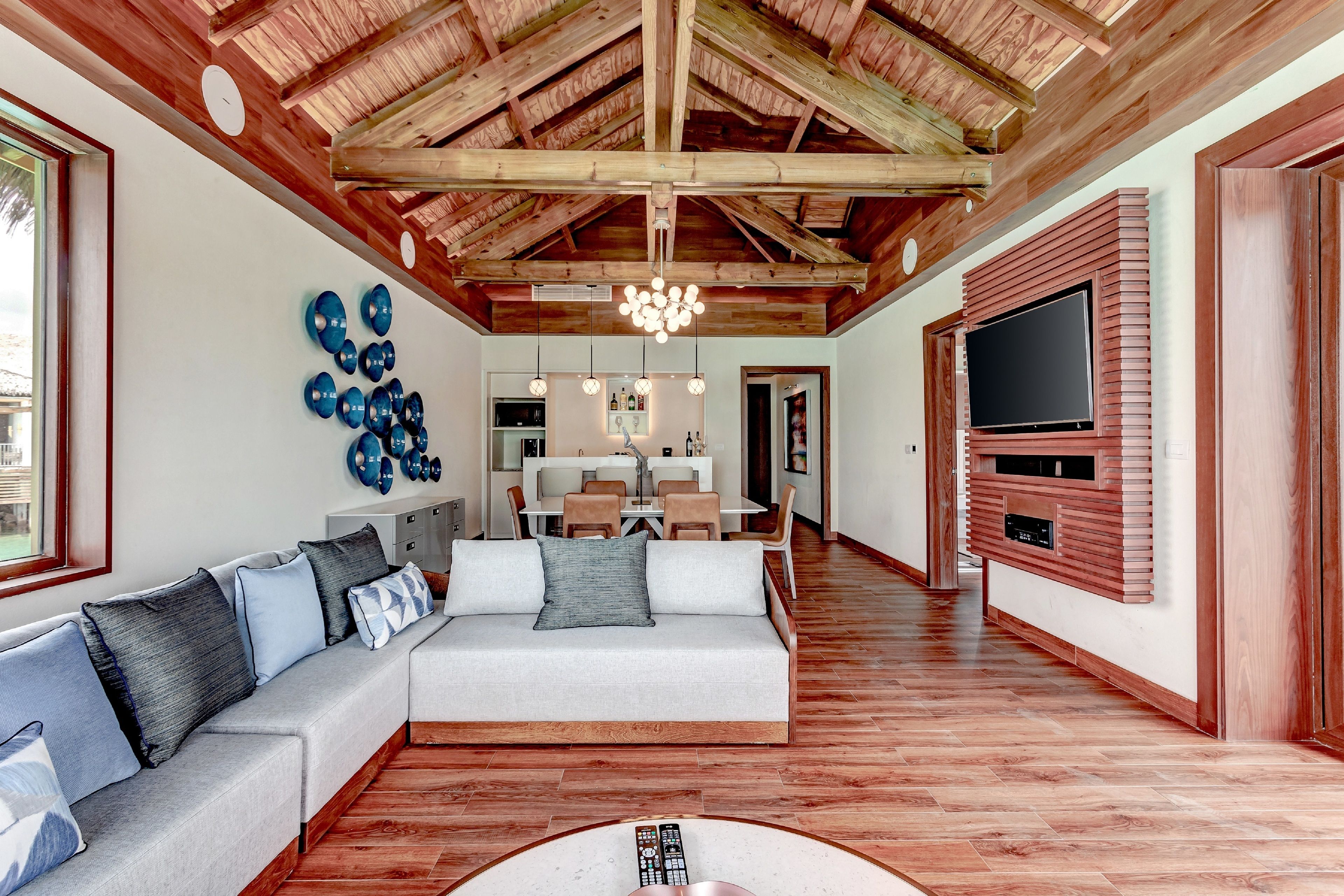 Un salón amplio con techo alto, vigas de madera, un televisor grande y un sofá moderno.