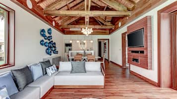 Un salón amplio con techo alto, vigas de madera, un televisor grande y un sofá moderno.