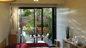A bedroom with a bed, a TV, a desk, and a view of a garden through a sliding door. - Urbanhouse Cocoon Studio (Toulouse)