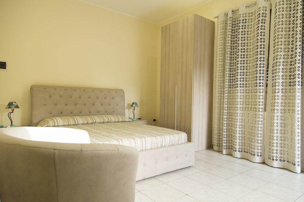 A bedroom with a bed, a nightstand, a lamp, and a curtain.