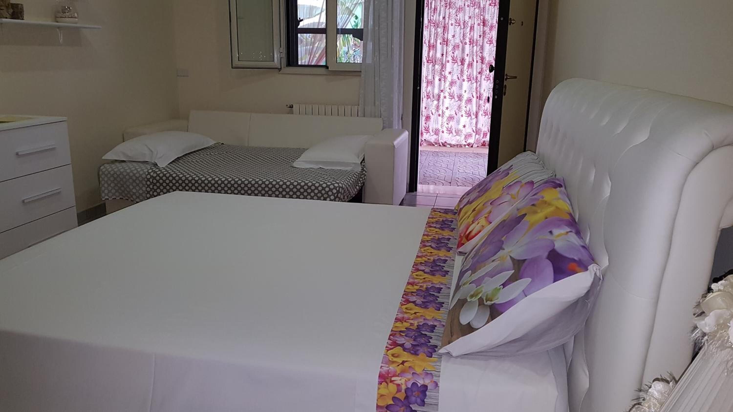 A bedroom with a large bed, a smaller bed, a dresser, and a window with curtains.