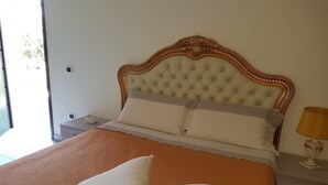 Ein Schlafzimmer mit einem großen Bett, einem Nachttisch, einer Lampe und Blick ins Freie.