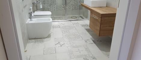 Une salle de bain comprenant des toilettes, un bidet et un lavabo, un carrelage décoratif au sol et un espace douche.