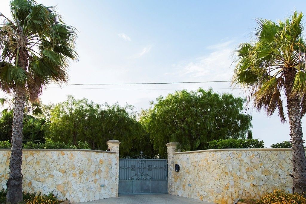 A gated entrance with a stone wall and palm trees.