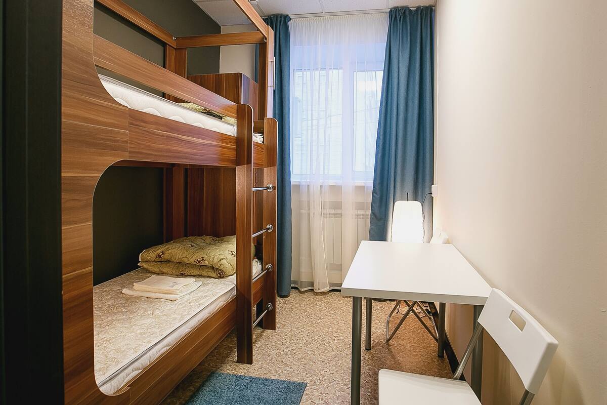 Ein Etagenbett mit Schreibtisch und Stuhl, ein Fenster mit Vorhängen und ein Teppichboden.