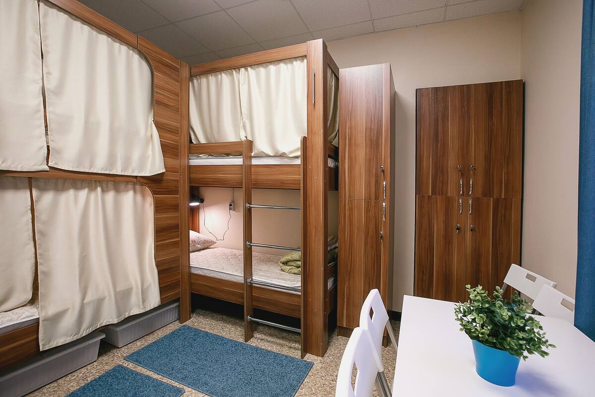 Ein Stockbett mit Vorhängen, ein Kleiderschrank und ein kleiner Tisch mit einer Pflanze.