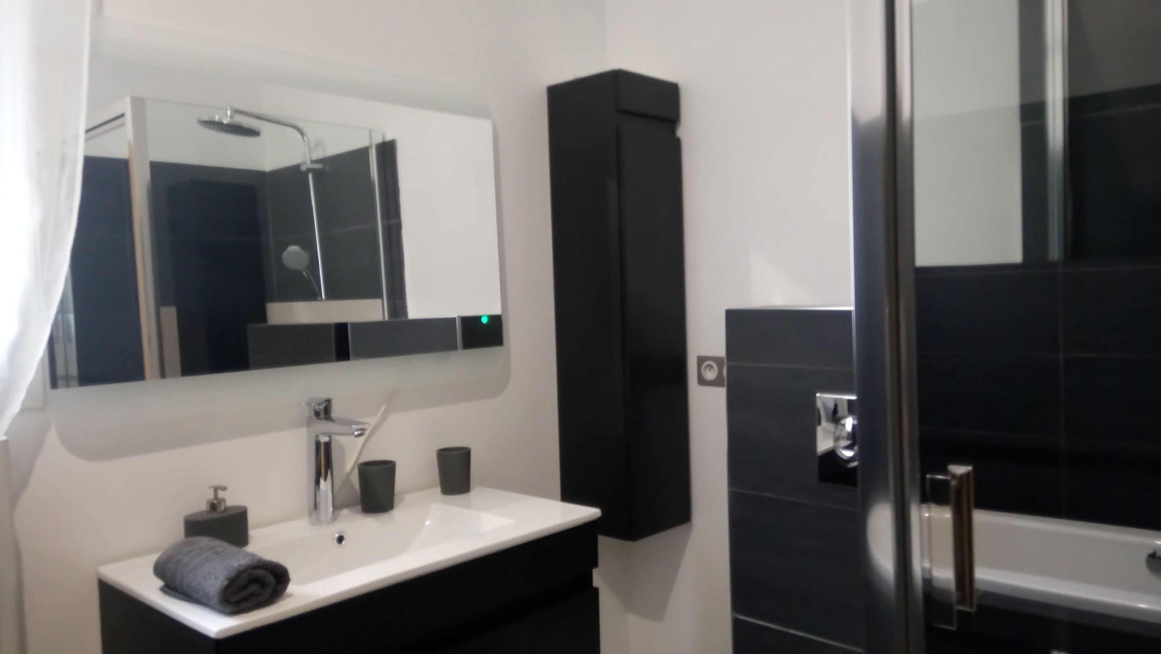 A modern bathroom with a white sink, a mirror, a black cabinet, and a glass shower enclosure.