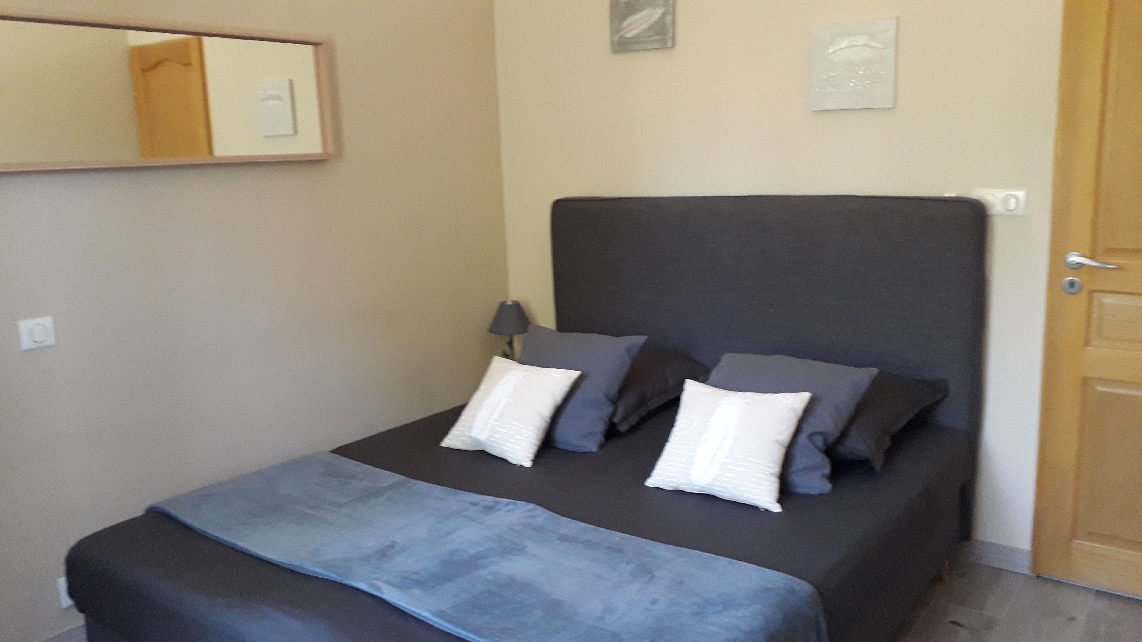 A small, neatly made bed with a dark headboard, a bedside lamp, and a mirror on the wall.