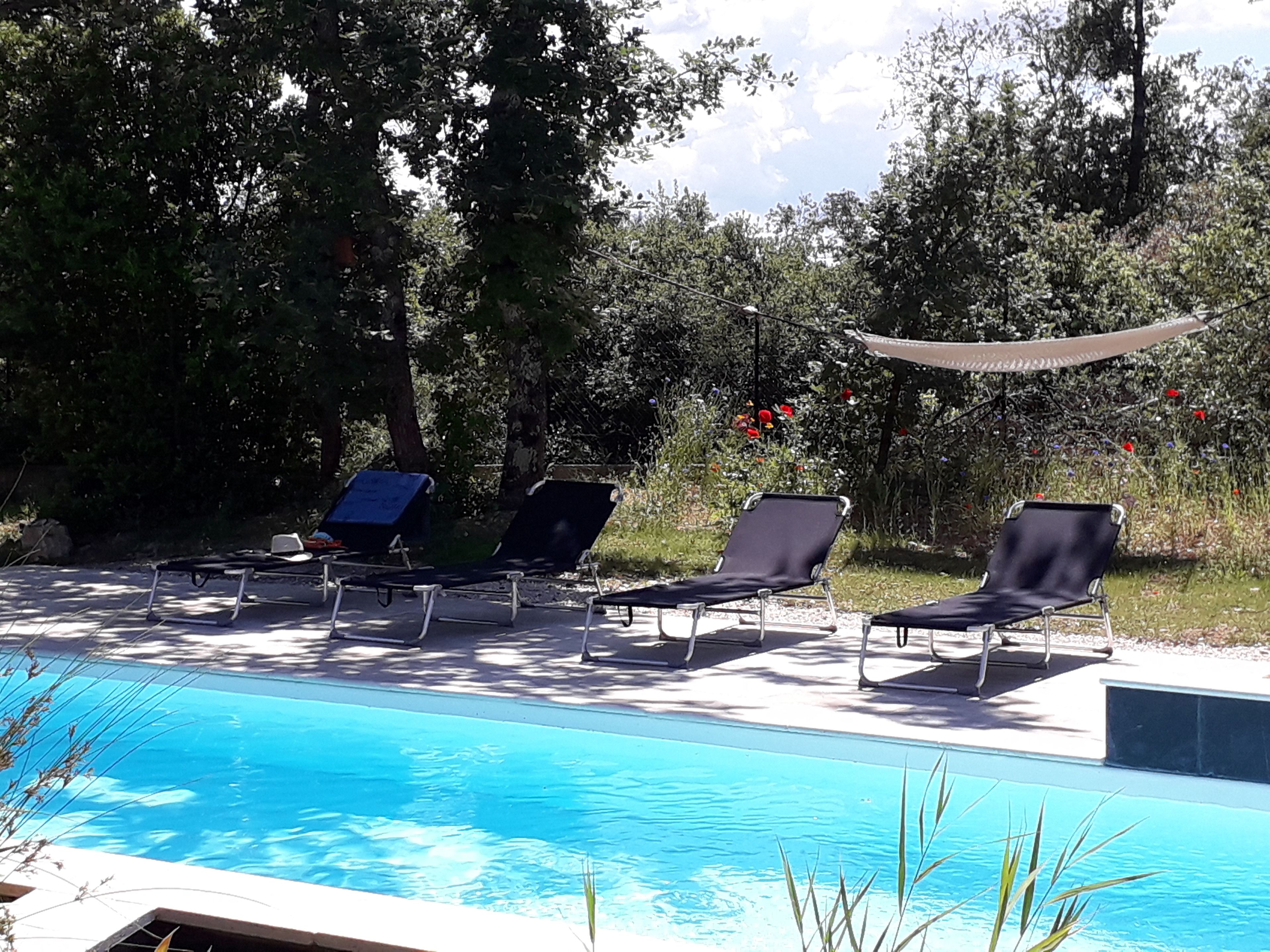 Een zwembadterras met ligbedden en een zonnescherm.