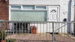 En hvid bygning med garageport, lille veranda med gelænder og en potteplante.