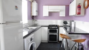Une cuisine compacte équipée d’un lave-linge, d’une cuisinière, d’un four à micro-ondes et de deux tabourets.