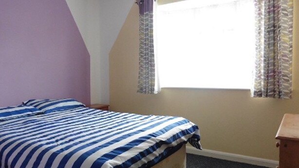 A bedroom with a bed, a window with curtains, and a wooden nightstand. - Leysdown Chalet 36 (Sheerness)