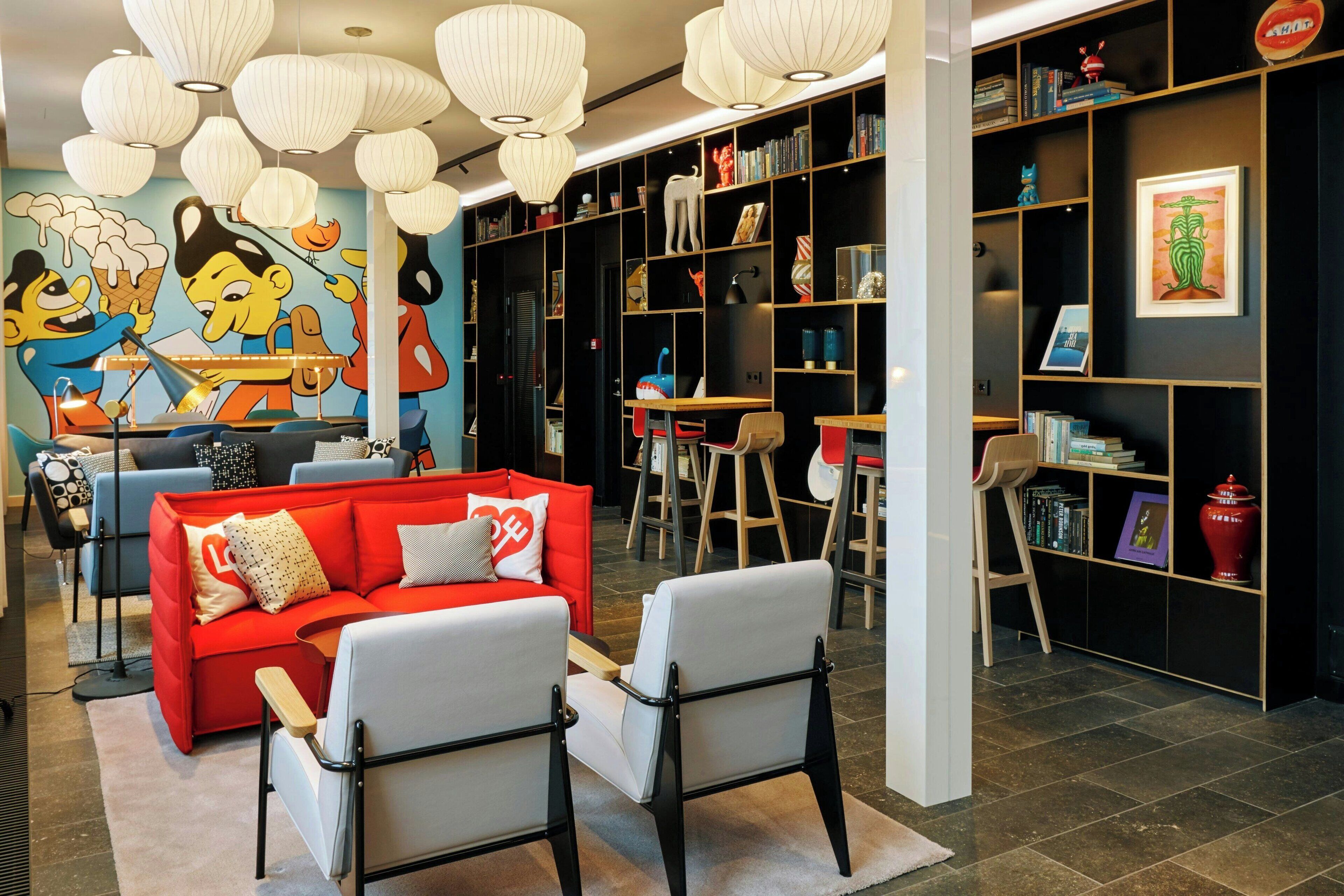 A modern living room with a red sofa, white armchairs, a mural, and a bookshelf.