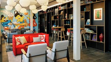 A modern living room with a red sofa, white armchairs, a mural, and a bookshelf.