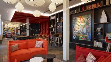 Un interior moderno con sofás rojos, un comedor y una estantería con libros y objetos decorativos.