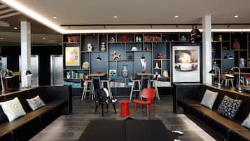 Ein moderner Lounge-Bereich mit schwarzen Sofas, roten und schwarzen Sesseln, einem schwarzen Couchtisch und einem Bücherregal voller Bücher und Dekoration.