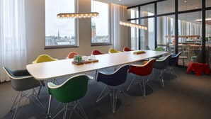 Ein moderner Konferenzraum mit einem langen Tisch, bunten Stühlen und großen Fenstern mit Blick auf die Stadt.