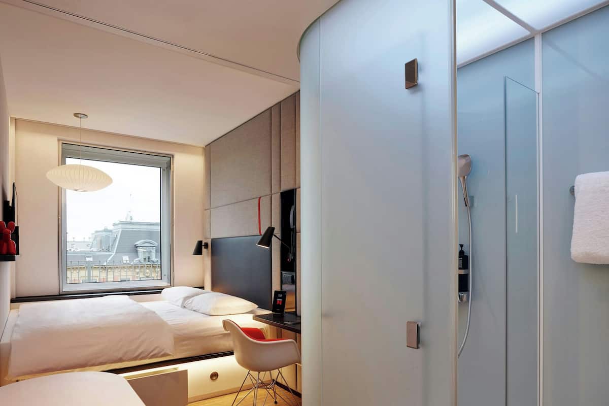 Ein modernes Hotelzimmer mit Bett, Schreibtisch, Stuhl, Fernseher und Duschbereich.