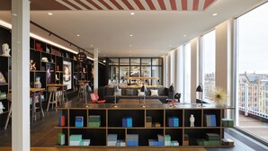 Eine moderne Bibliothek mit Bücherregalen, Sitzbereichen und großen Fenstern mit Blick auf die Stadt.