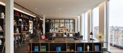 A modern library with bookshelves, seating areas, and large windows offering views of the city.