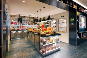 Un espace cuisine moderne doté d’un îlot central où sont rangés divers aliments et ustensiles, d’un éclairage suspendu et d’une disposition épurée et bien organisée.