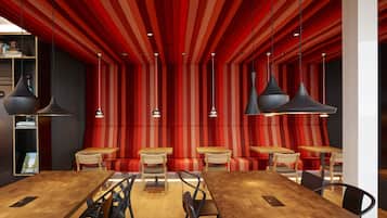 Interior de restaurante moderno con paredes a rayas rojas y negras, mesas y sillas de madera, e iluminación colgante.