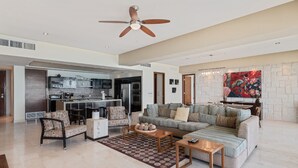 A spacious living area with a sofa, coffee table, and chairs, a kitchen in the background, and a ceiling fan. - Encanto Living 1103 -3BR by Kivoya (Puerto Peñasco)