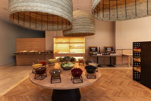 Uma área de refeições com uma mesa redonda central rodeada por várias tigelas de comida, um buffet ao fundo e um candeeiro tecido pendurado.
