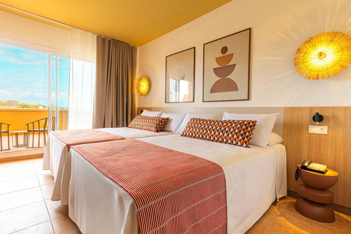Ein Hotelzimmer mit zwei Betten, einem Balkon, einer Wandleuchte und einem Holznachttisch mit Telefon.