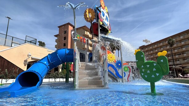 Un área de juegos con agua, con un tobogán azul y una fuente.