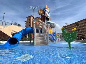 Un área de juegos con agua, con un tobogán azul y una fuente.