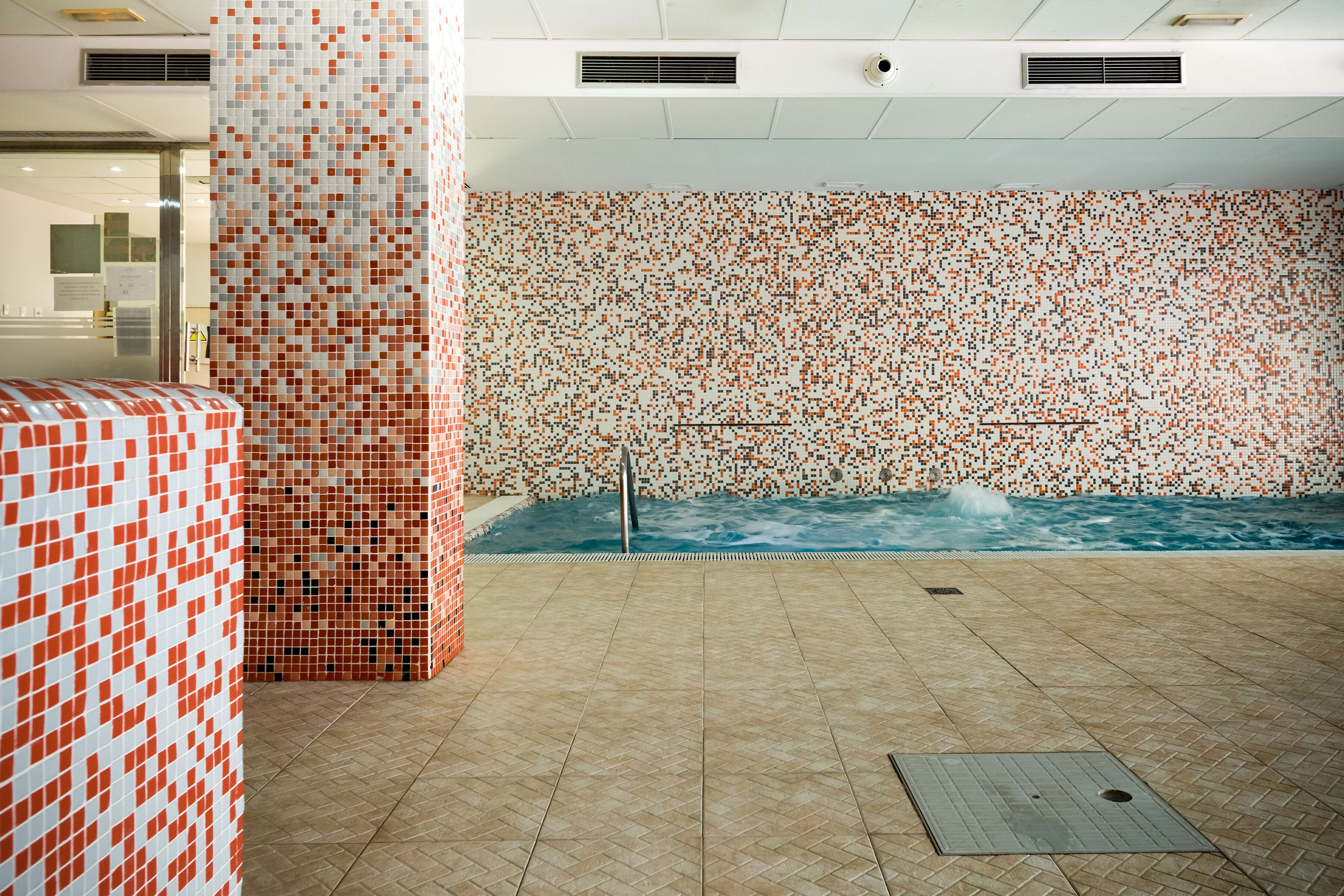 A spa area with a tiled wall, a pool, and a tiled floor.