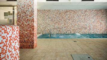 A spa area with a tiled wall, a pool, and a tiled floor.