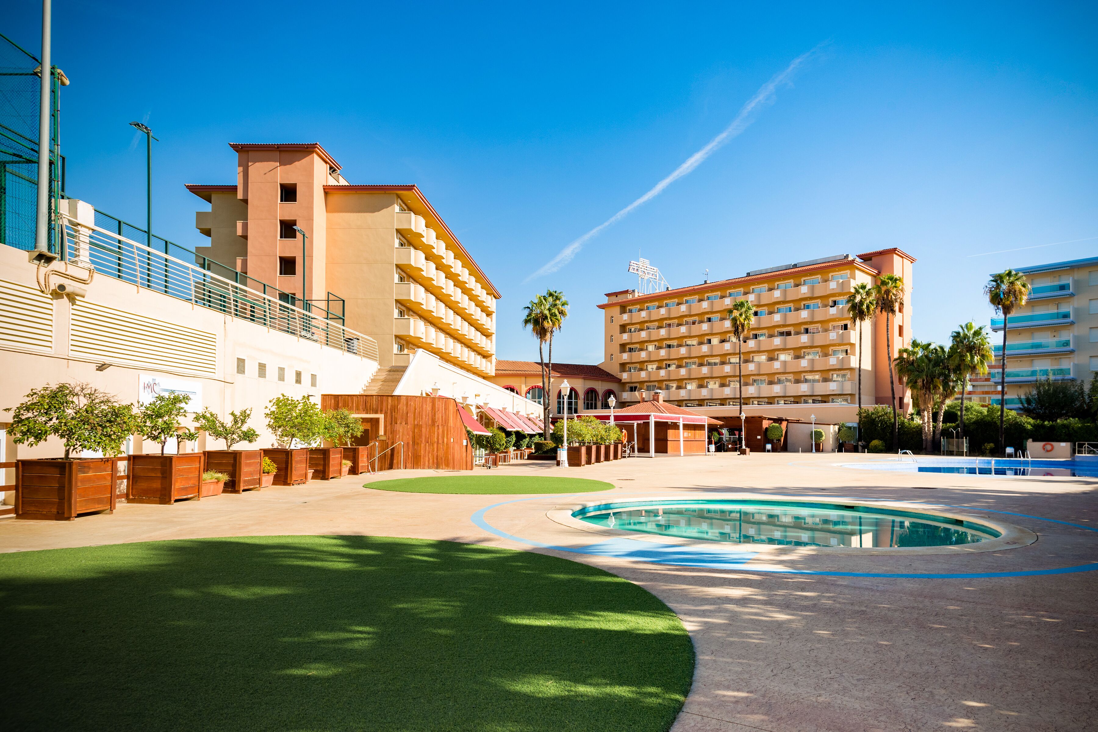 Une cour d’hôtel avec une piscine, des palmiers et un bâtiment doté de nombreux balcons.
