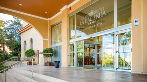 La entrada del Gran Hotel La Hacienda, con fachada de vidrio, un área de acceso cubierta y una escalera que conduce al interior.