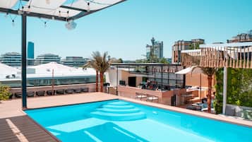Una piscina en la azotea con zona de bar, asientos y vistas al horizonte de la ciudad.