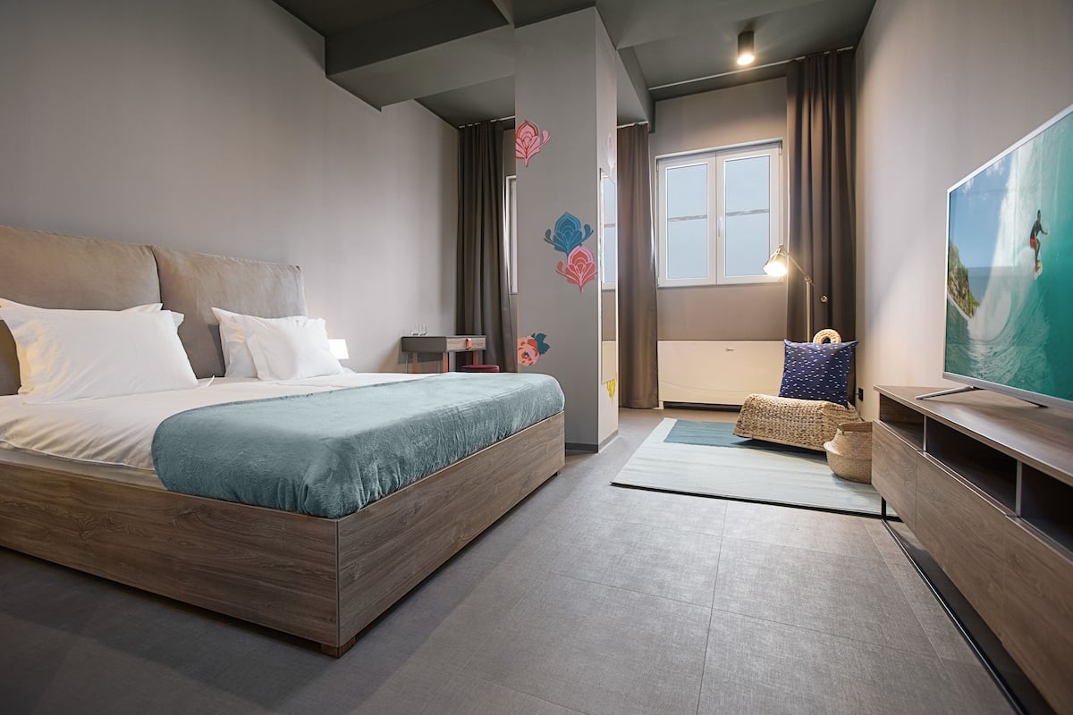 A modern hotel room with a large bed, a television, and a view of the ocean.