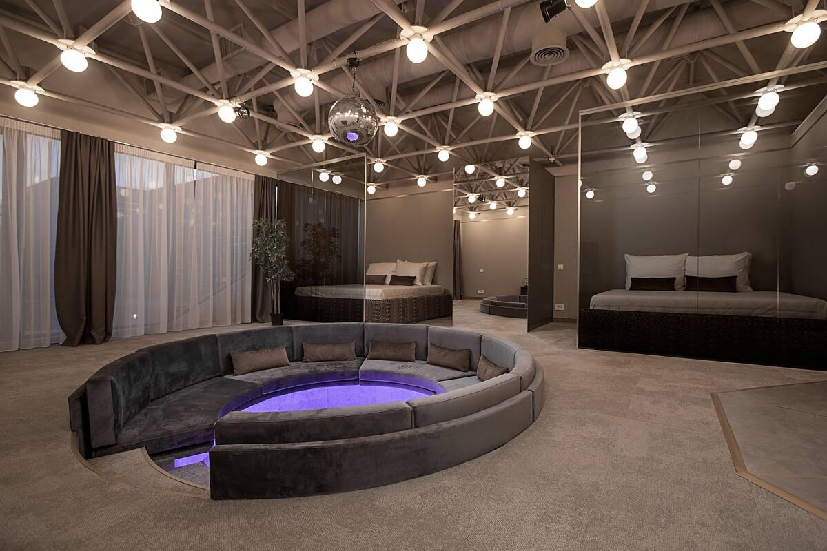 A modern, well-lit room with a circular seating area, a bed, and a large mirror.