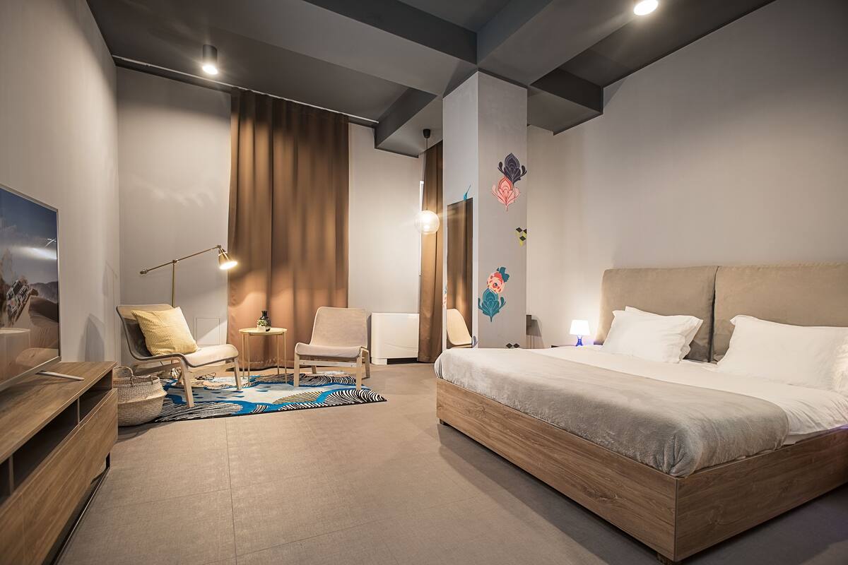A modern hotel room with a large bed, a desk, two chairs, and a TV.