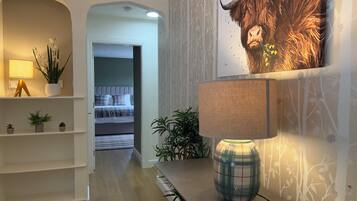 A hotel hallway with a bed, a lamp, and a wall with a tree pattern.