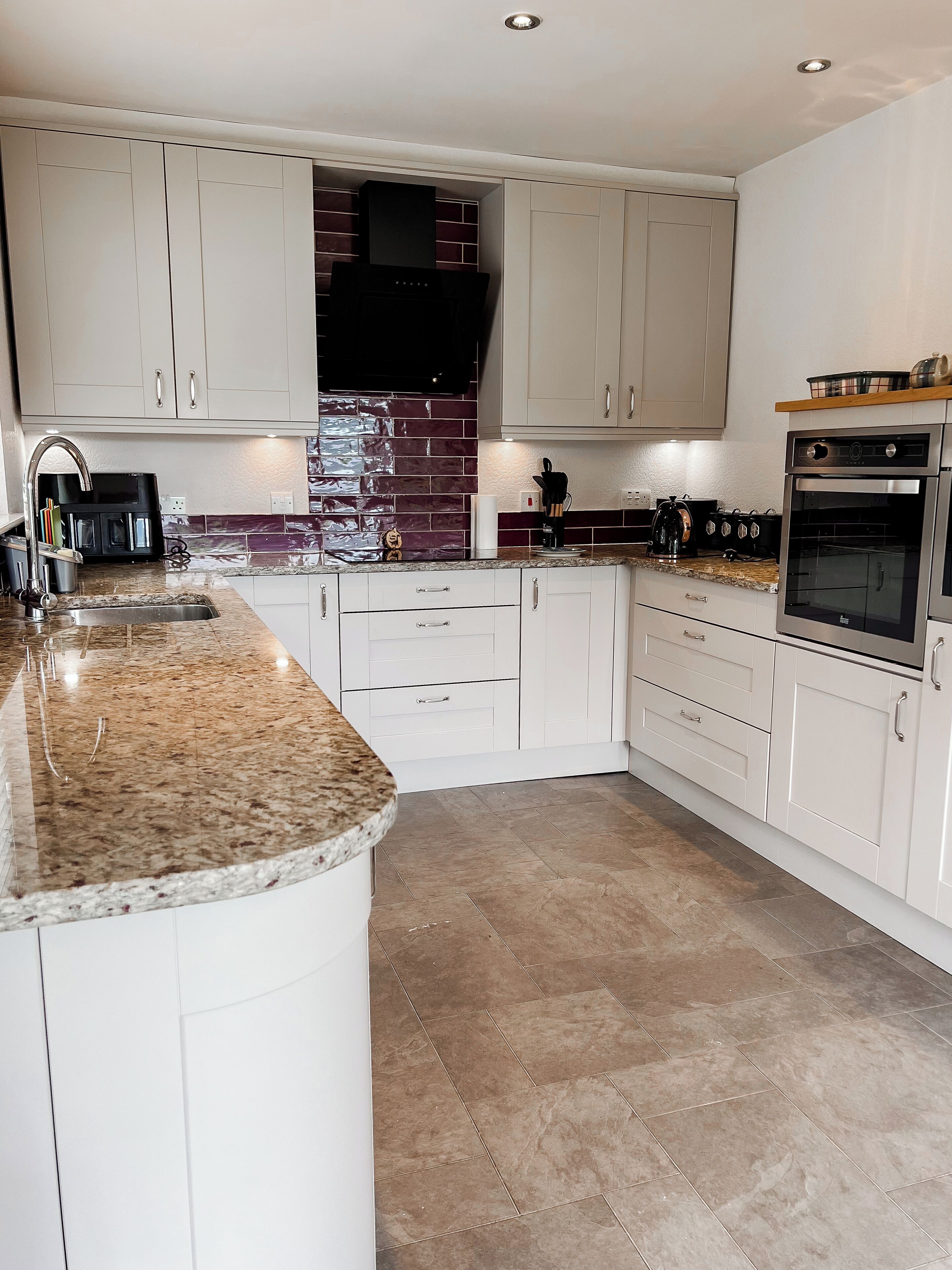A modern kitchen with white cabinets, a granite countertop, a built-in oven, and a brick backsplash.
