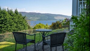 An outdoor seating area with two chairs and a table, overlooking a lake and mountains. - Loch Ness Cottages (Inverness)