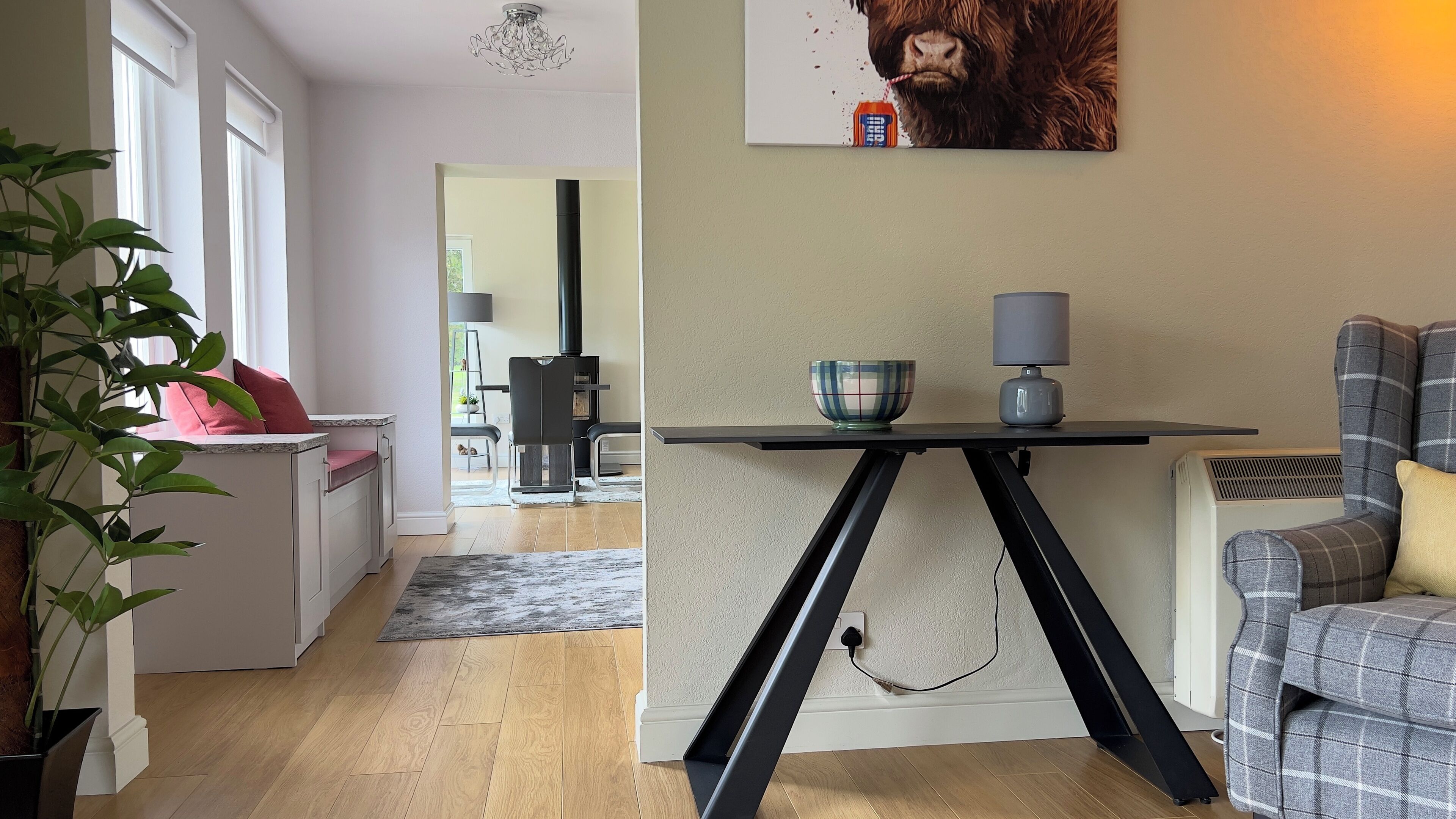 Een moderne woonkamer met een eethoek, een zwarte tafel met een schaal en een lamp, en een grijze bank.