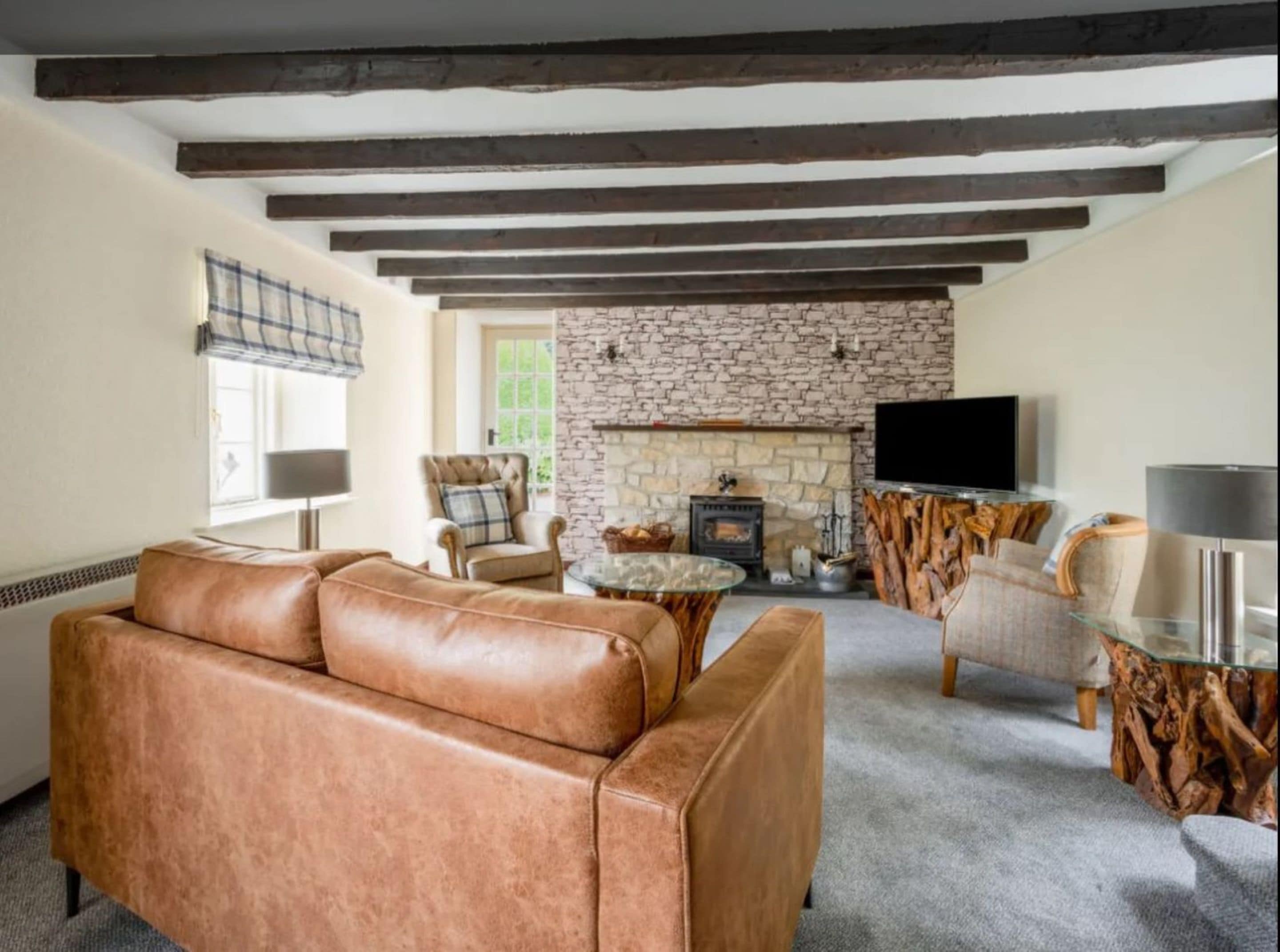 A cozy living room with a stone fireplace, leather sofa, and rustic wooden beams.