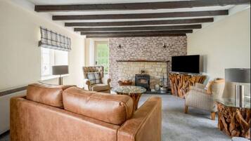 A cozy living room with a stone fireplace, leather sofa, and rustic wooden beams.