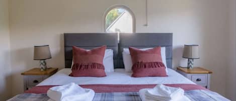 A neatly made bed with two pillows, two bedside tables with lamps, and a window with a view of the outside.