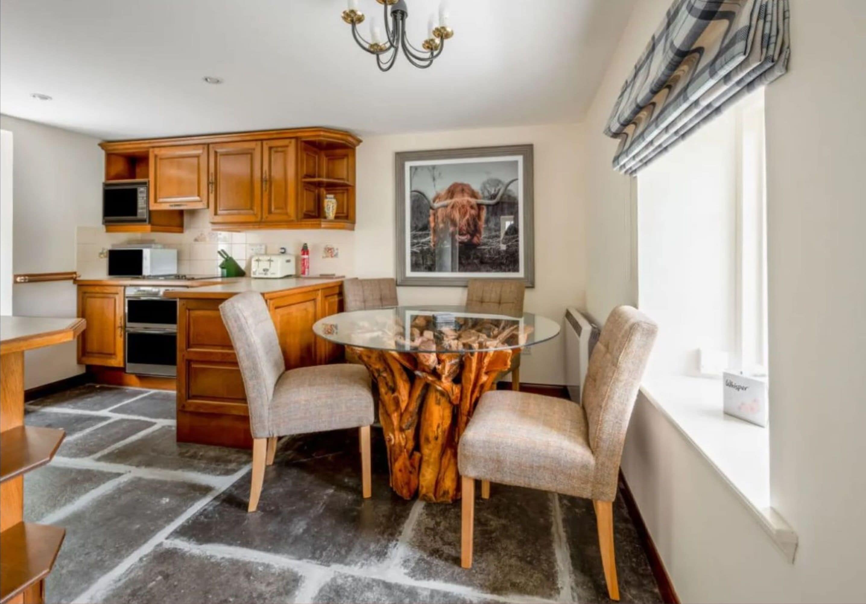 A kitchen with wooden cabinets, a microwave, and a glass table with chairs.