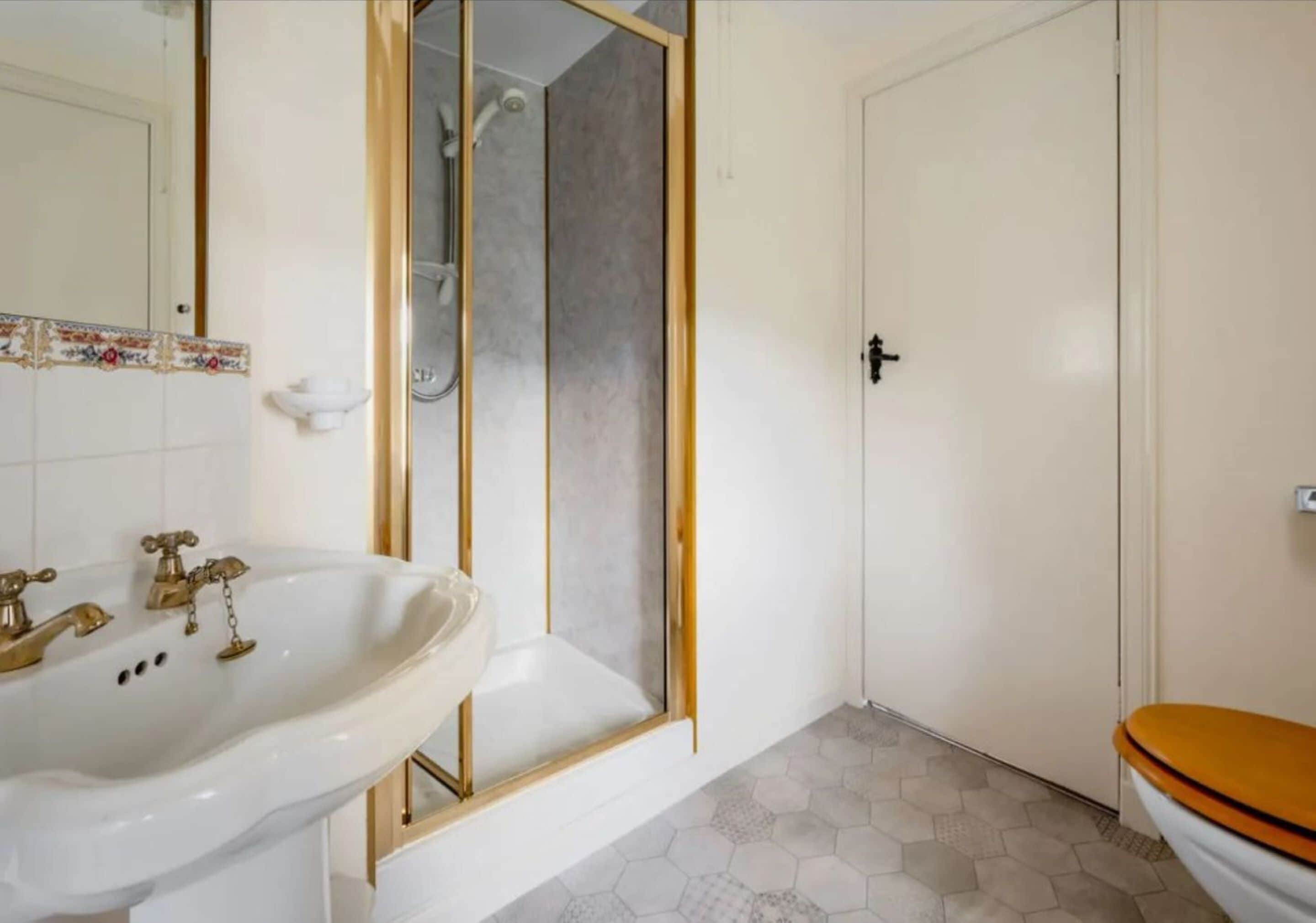A bathroom with a white sink, a shower with a glass door, and a toilet with a wooden seat.