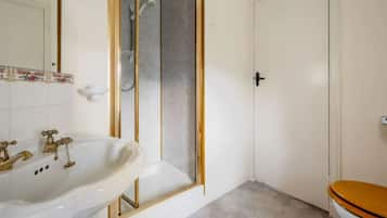 A bathroom with a white sink, a shower with a glass door, and a toilet with a wooden seat.