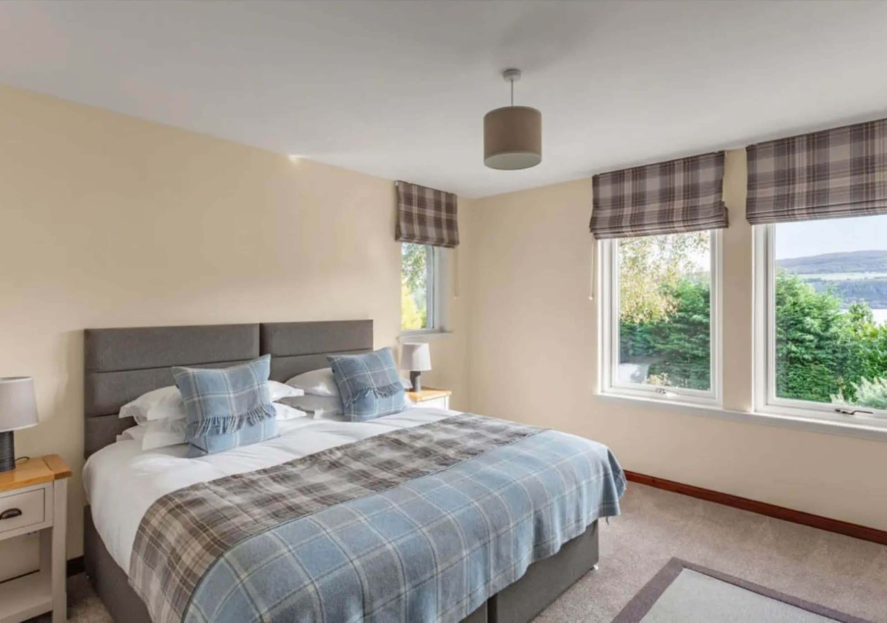 A bedroom with a bed, nightstands, a window with curtains, and a view of greenery outside.
